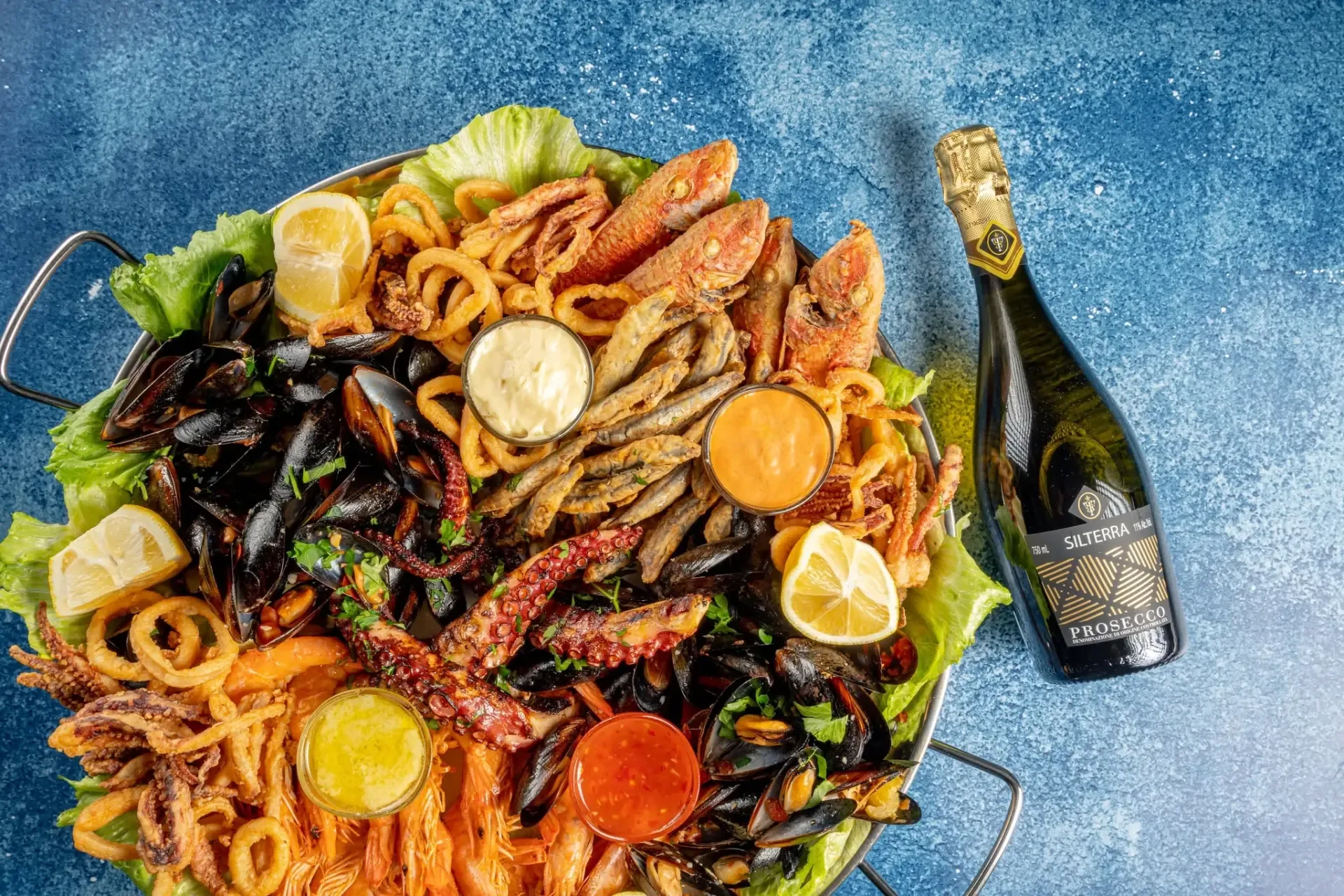 Platou mare cu fructe de mare: midii, caracatiță la grătar, inele de calamar, creveți, peștișori prăjiți, barbun, lămâie și sosuri
